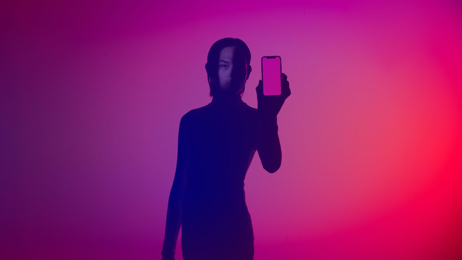 DMEXCO column: Evgeny Popov on AI agents as intelligent decision-makers AI agents: A person in shadow holds a smartphone up to the camera against a colorful gradient background in shades of pink and violet