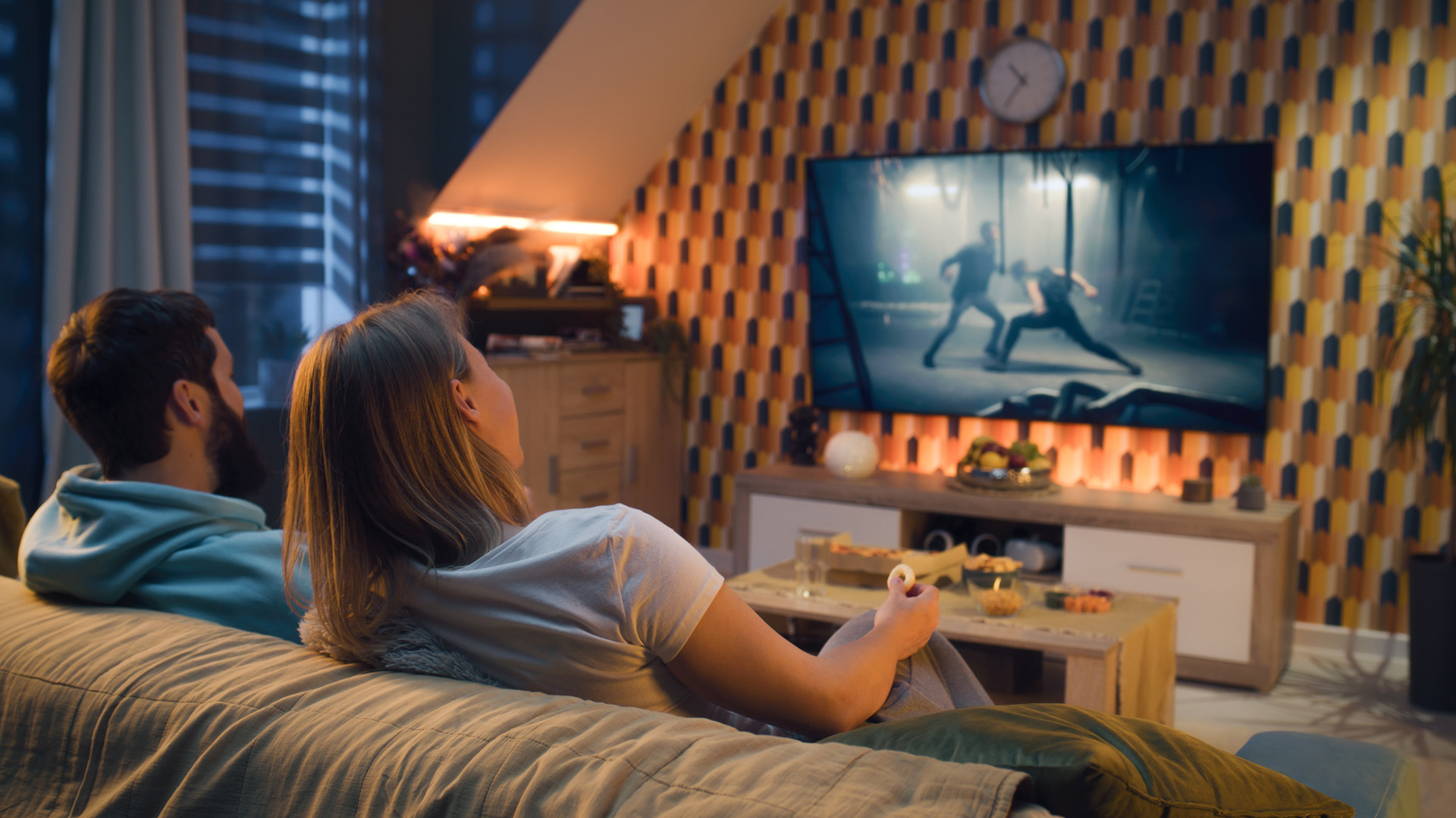 CTV Advertising wird relevanter denn je. CTV Advertising: Ein Mann und eine Frau sitzen im Wohnzimmer auf dem Sofa und schauen einen Werbeclip auf dem Fernseher an.