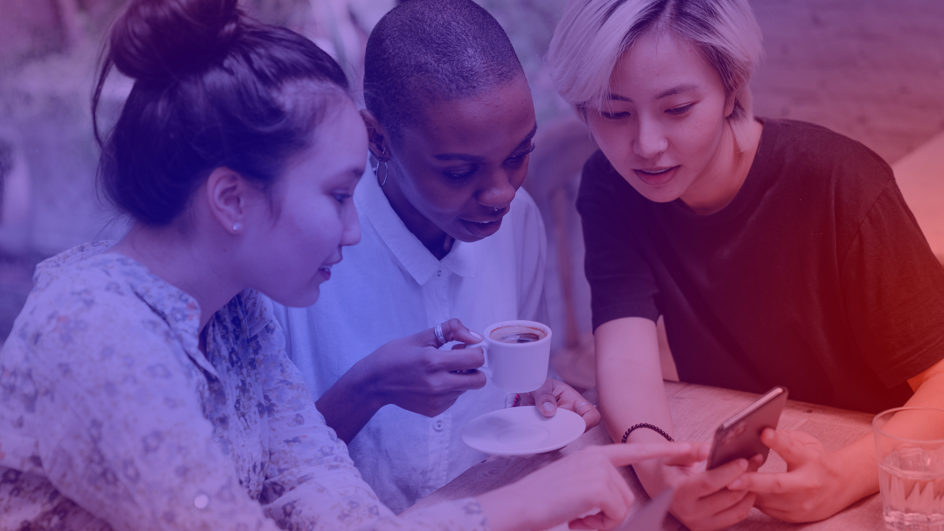 Social Commerce im Alltag: Kund:innen entdecken Produkte direkt auf dem Smartphone. Drei junge Frauen betrachten gemeinsam ein Smartphone: Social Commerce in der Anwendung beim gemeinsamen Kaffee.