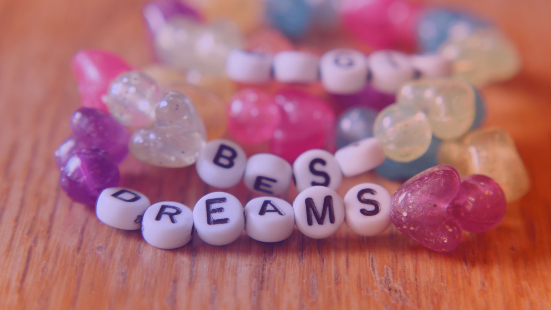 Taylor Swifts Marketing-Strategie sichert ihr globale Relevanz. Großaufnahme bunter Perlenarmbänder mit Herzen und Buchstaben, die den Schriftzug \'Best Dreams\' zeigen – kreative Darstellung im Kontext von Taylor Swifts Marketing.
