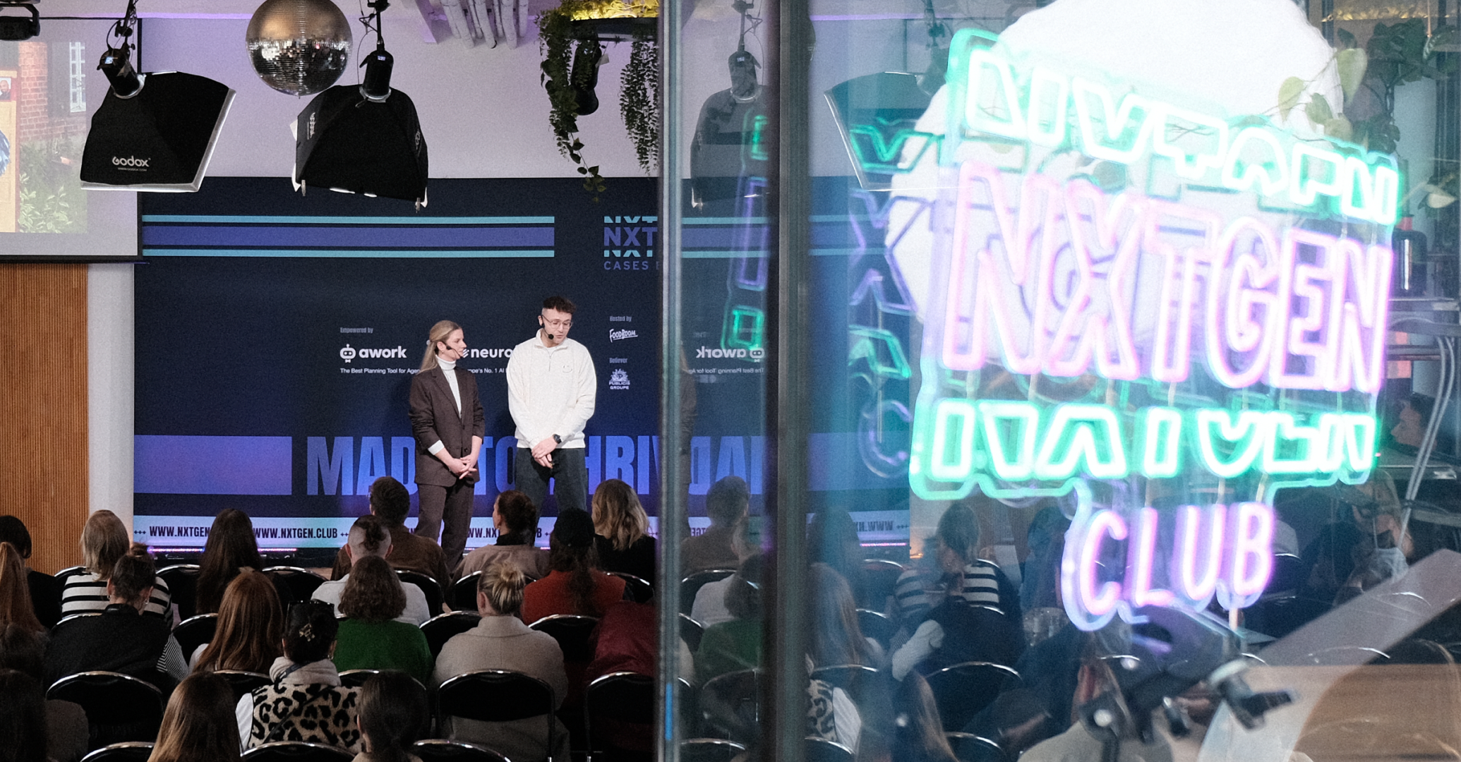 Speaker:innen auf der Bühne von NXTGEN Cases vor Publikum mit beleuchtetem NXTGEN Club Branding im Vordergrund.